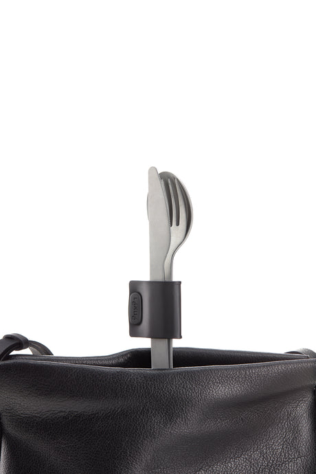 Set of silverware; knife, fork and spoon. The three utensils are held together by a black clasp as they sit standing upright in a black bag.