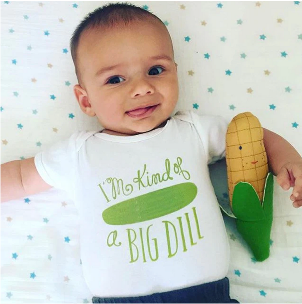 Small toddler lays on starry background with white onesie with pickle on it that reads 