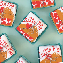 Load image into Gallery viewer, Egg cartons with white onesie that read &quot;Cutie pie&quot; in red with image of pie below are laid out on green background and tied up with string