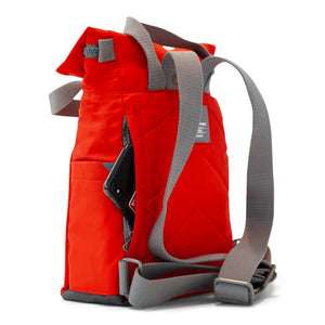 Side view of red ORI bag with gray back straps and open side zipper pocket with phone sticking out on white background